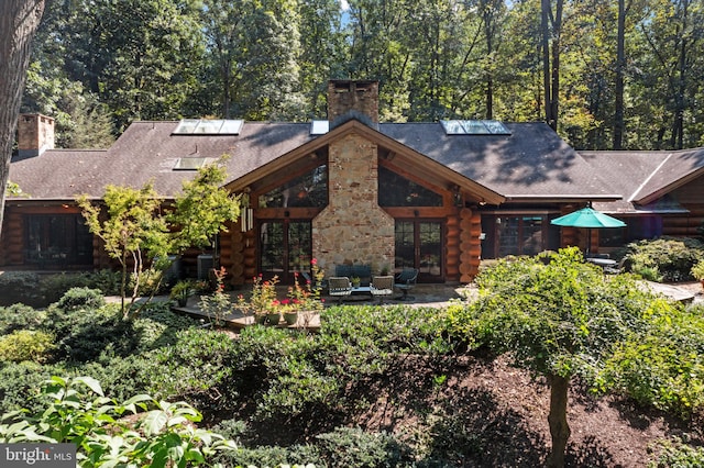 exterior space featuring log siding, a chimney, french doors, a patio area, and a shingled roof