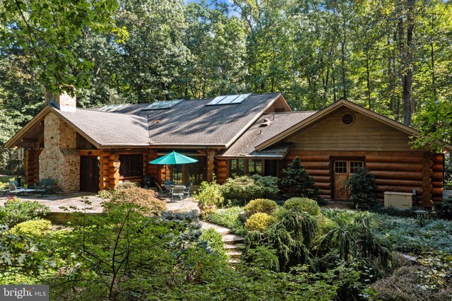 rear view of house featuring log siding, a patio, a chimney, and a shingled roof