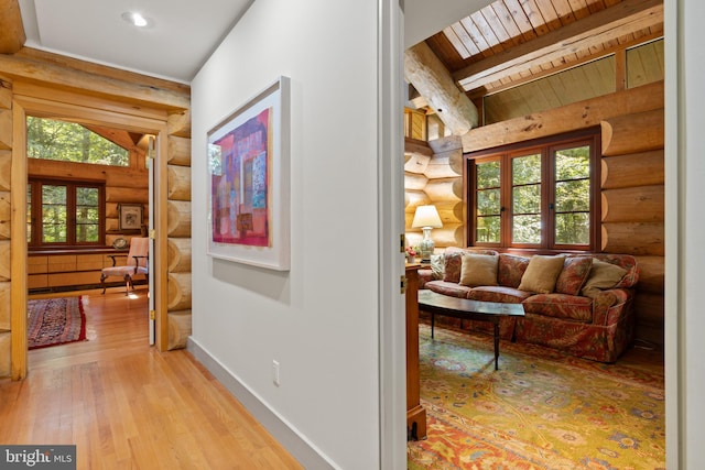 hallway with beamed ceiling, light wood-style flooring, wooden ceiling, and rustic walls