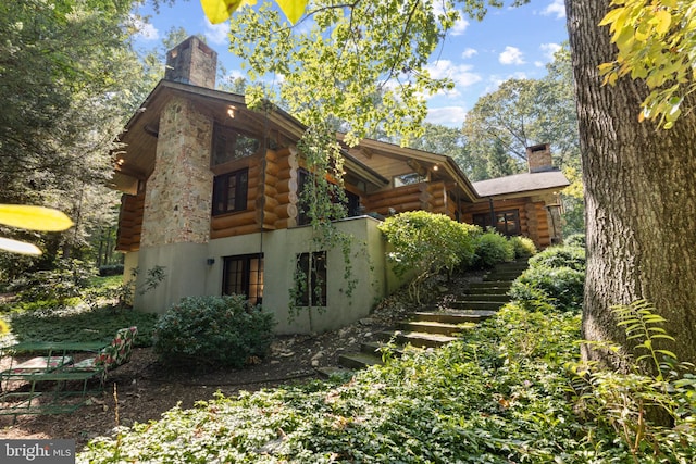 view of property exterior with log siding, a chimney, and stairs
