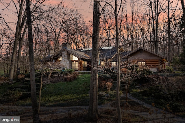 property exterior at dusk with log siding, a chimney, and metal roof