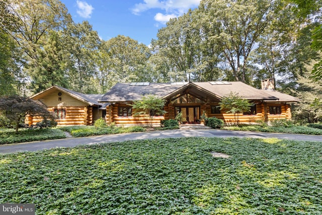 cabin featuring a chimney, driveway, french doors, a front yard, and log exterior