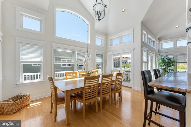 dining space with a towering ceiling, a chandelier, and light wood-type flooring