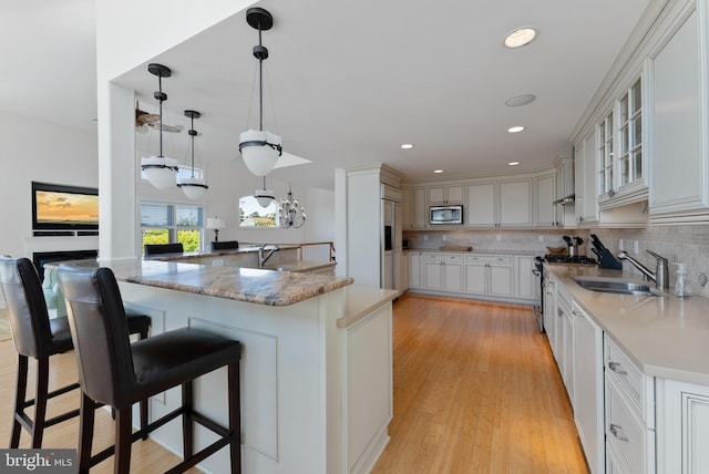 kitchen featuring built in appliances, white cabinets, a kitchen bar, and decorative light fixtures