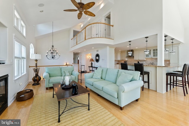 living room with ceiling fan with notable chandelier, light hardwood / wood-style flooring, and a high ceiling