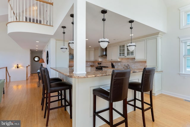 kitchen with wall chimney exhaust hood, gas stove, hanging light fixtures, and light wood-type flooring