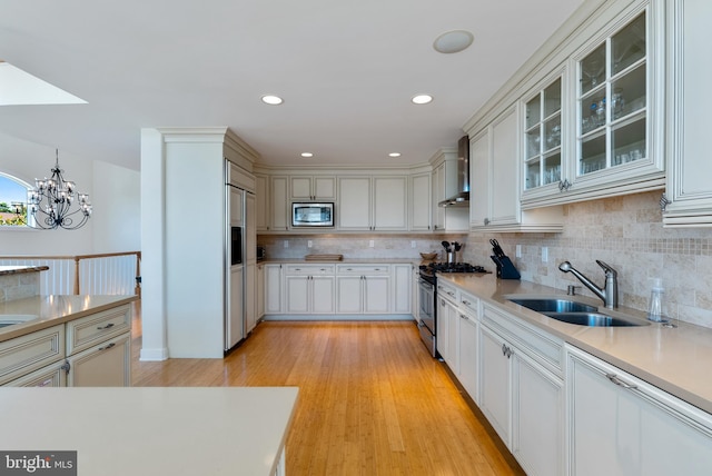 kitchen with pendant lighting, sink, backsplash, built in appliances, and wall chimney exhaust hood