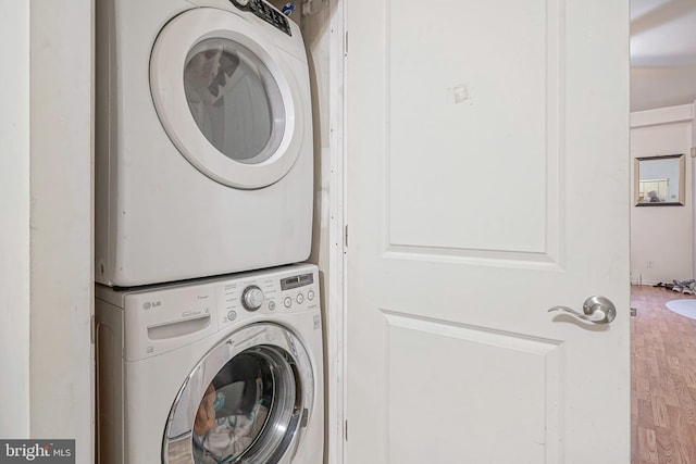 washroom with stacked washer / drying machine and hardwood / wood-style flooring