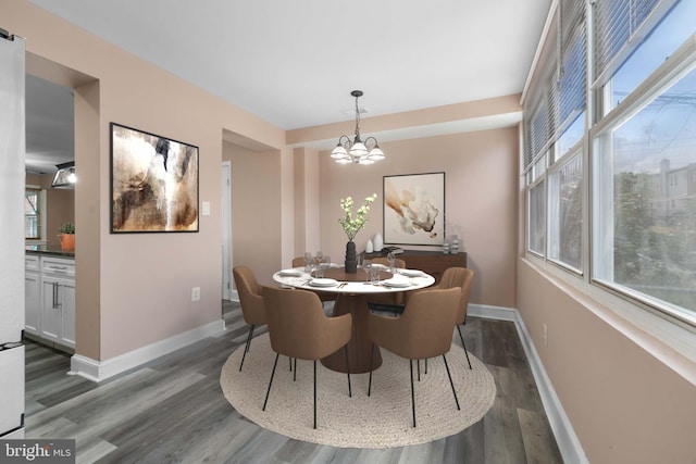 dining space with dark wood-style flooring, a notable chandelier, and baseboards