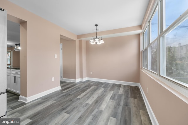 unfurnished dining area featuring a notable chandelier, dark wood-style flooring, and baseboards