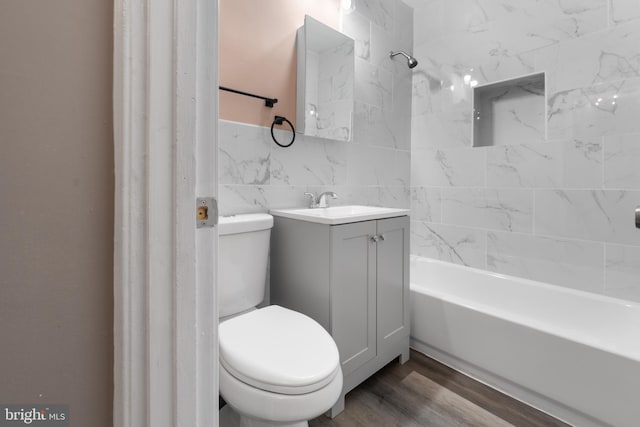 full bathroom featuring hardwood / wood-style flooring, tiled shower / bath combo, vanity, tile walls, and toilet