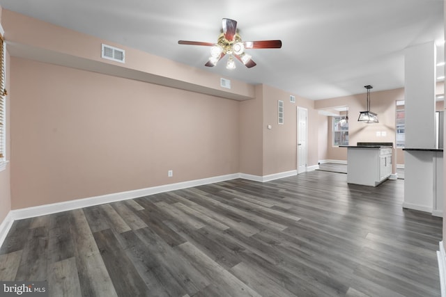 unfurnished living room featuring a ceiling fan, baseboards, visible vents, and dark wood-type flooring