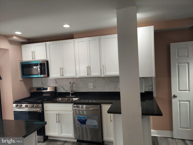 kitchen featuring hardwood / wood-style floors, white cabinetry, sink, dark stone countertops, and stainless steel appliances