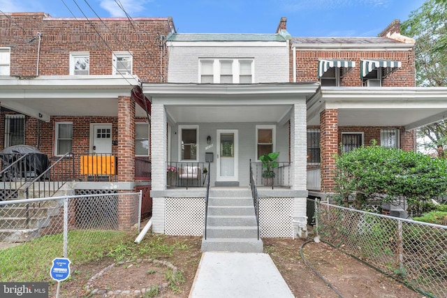 townhome / multi-family property with covered porch, a fenced front yard, and brick siding