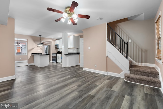 unfurnished living room featuring stairs, dark wood-style flooring, a ceiling fan, and baseboards