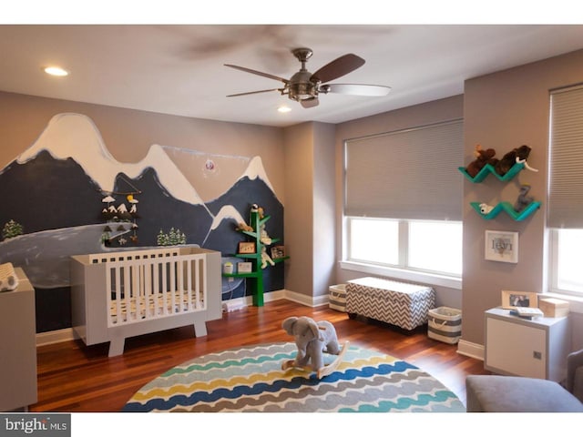 bedroom with hardwood / wood-style floors, a nursery area, and ceiling fan