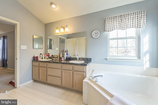 bathroom with tile patterned flooring, vanity, lofted ceiling, and tiled tub