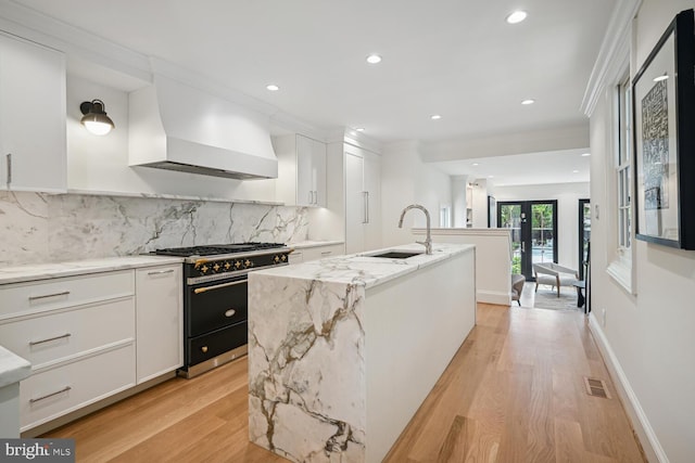 kitchen with white cabinets, a center island with sink, custom range hood, and high end stainless steel range