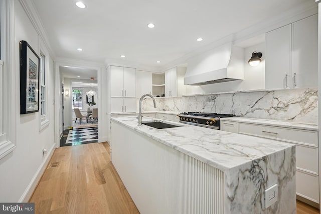 kitchen featuring white cabinets, light stone countertops, light hardwood / wood-style flooring, premium range hood, and stainless steel range