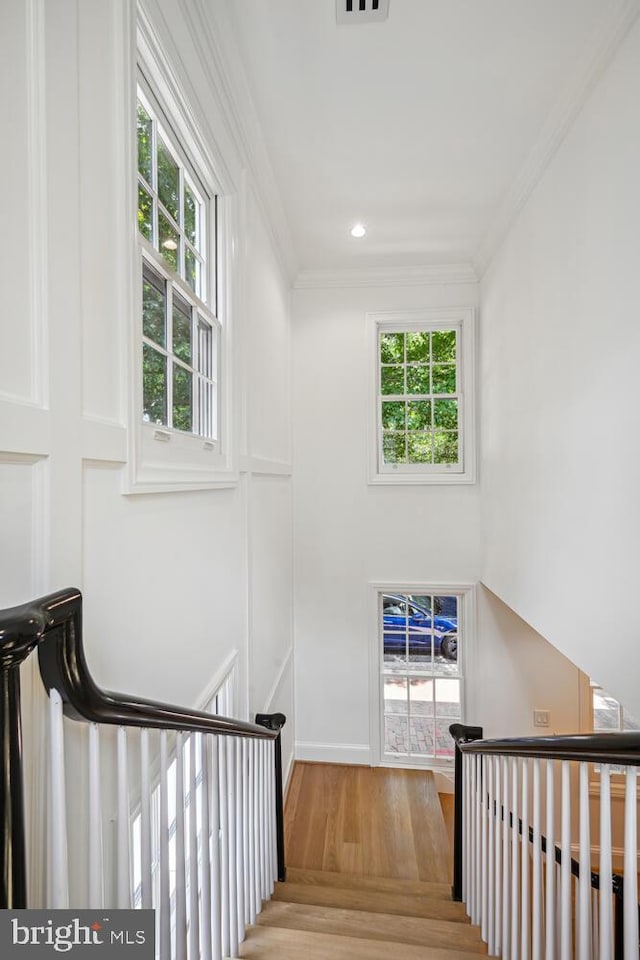 staircase with crown molding, hardwood / wood-style floors, and a healthy amount of sunlight