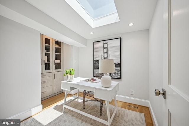 home office featuring light wood-type flooring and a skylight