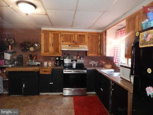 kitchen with brick wall, sink, a paneled ceiling, black fridge, and stainless steel range with electric cooktop