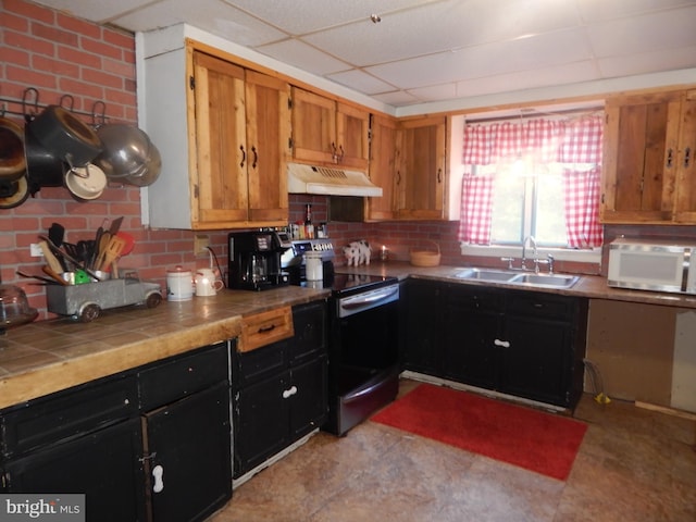 kitchen featuring a paneled ceiling, tile counters, sink, electric range, and brick wall