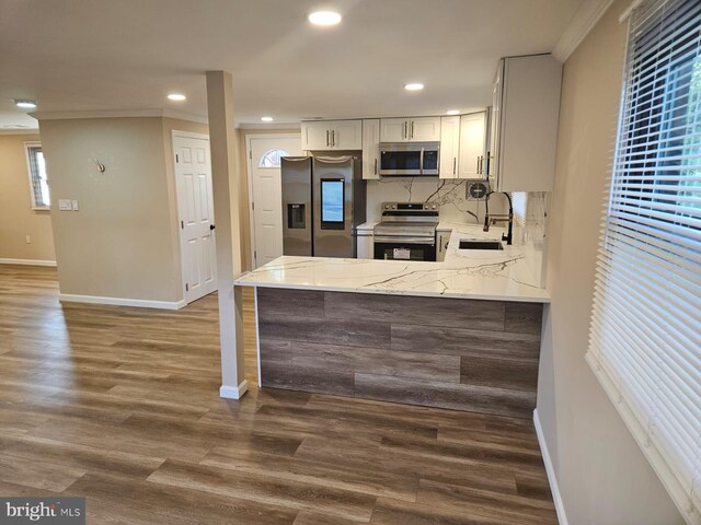 kitchen featuring appliances with stainless steel finishes, white cabinets, wood-type flooring, and backsplash