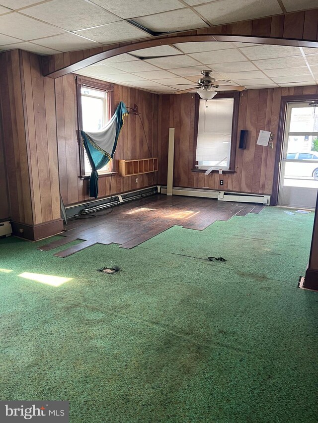 interior space featuring a drop ceiling, carpet, baseboard heating, and wood walls