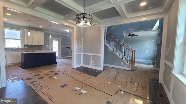 kitchen featuring coffered ceiling, a kitchen island, pendant lighting, white cabinets, and ceiling fan with notable chandelier