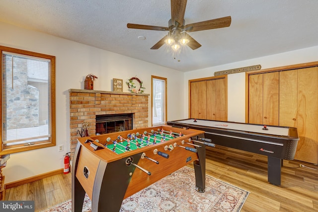 game room with a fireplace, ceiling fan, a textured ceiling, and light wood-type flooring