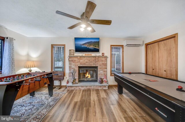 playroom with ceiling fan, an AC wall unit, pool table, a brick fireplace, and light hardwood / wood-style floors