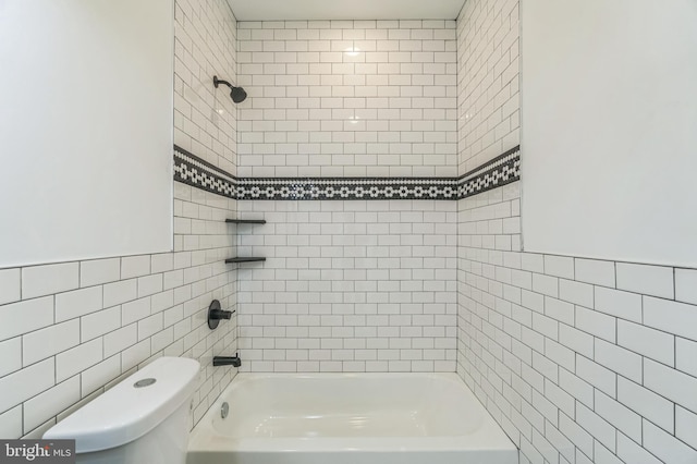 bathroom with toilet, tile walls, and tiled shower / bath