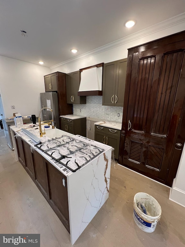 kitchen featuring an island with sink, backsplash, sink, custom exhaust hood, and light stone counters