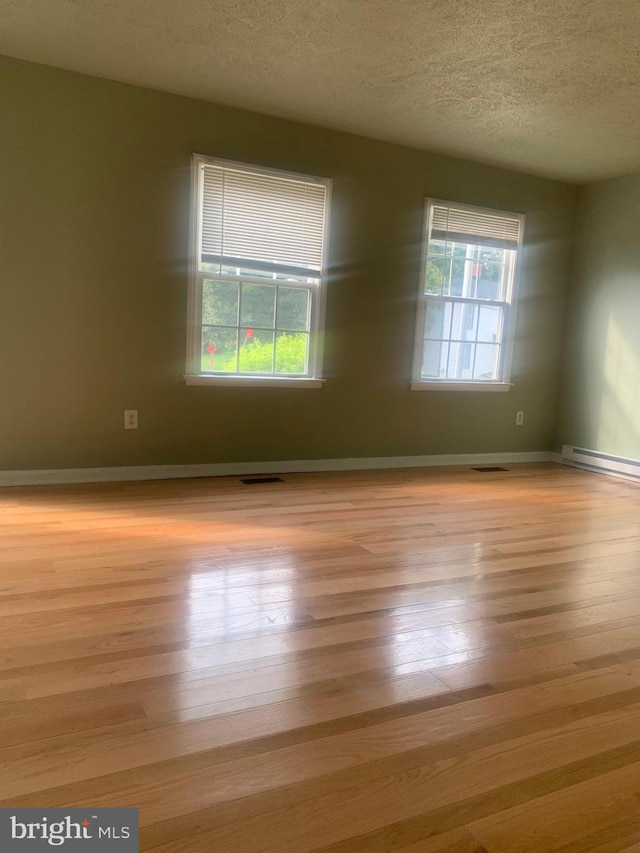 spare room with a wealth of natural light, a textured ceiling, baseboard heating, and light hardwood / wood-style flooring