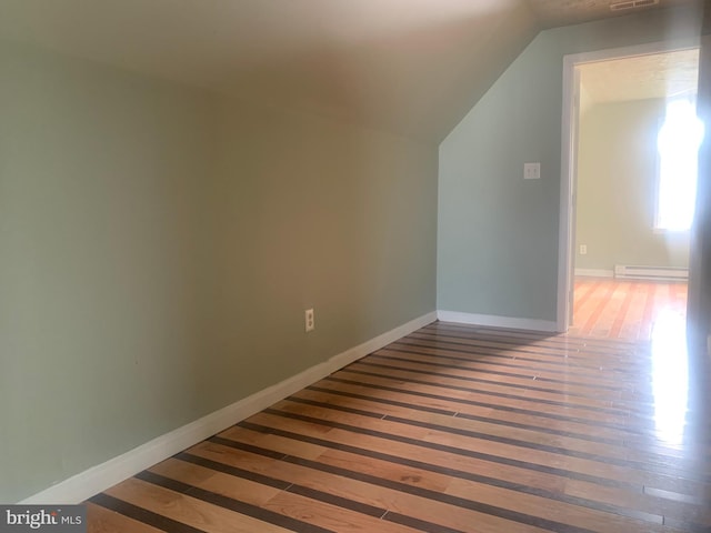 additional living space with lofted ceiling, a baseboard heating unit, and wood-type flooring