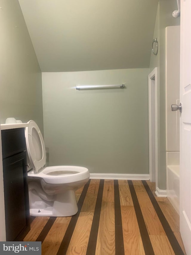 bathroom featuring a bathing tub, vaulted ceiling, hardwood / wood-style floors, vanity, and toilet