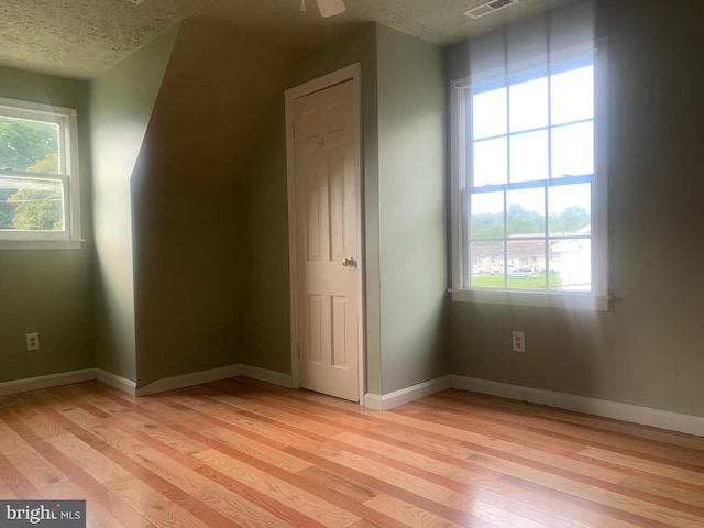 additional living space featuring ceiling fan, plenty of natural light, a textured ceiling, and light wood-type flooring