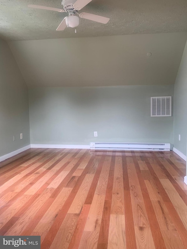 additional living space with hardwood / wood-style flooring, lofted ceiling, a textured ceiling, and a baseboard heating unit