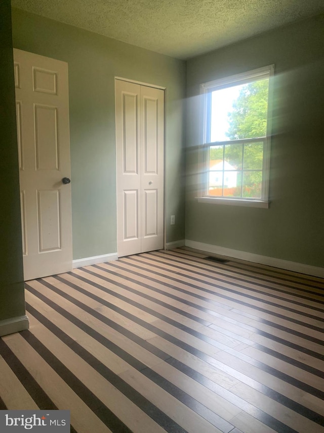 unfurnished bedroom featuring a textured ceiling, a closet, and hardwood / wood-style flooring