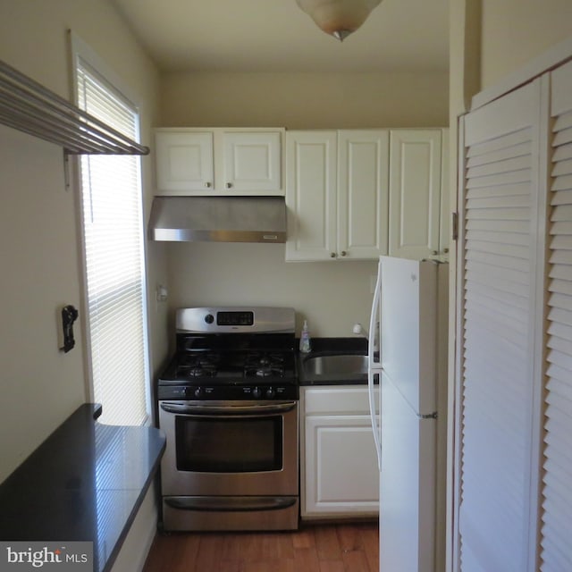 kitchen featuring wall chimney range hood, light hardwood / wood-style flooring, stainless steel range with gas stovetop, white cabinets, and white fridge