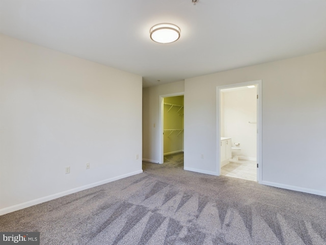 unfurnished bedroom featuring light carpet, a spacious closet, a closet, and connected bathroom