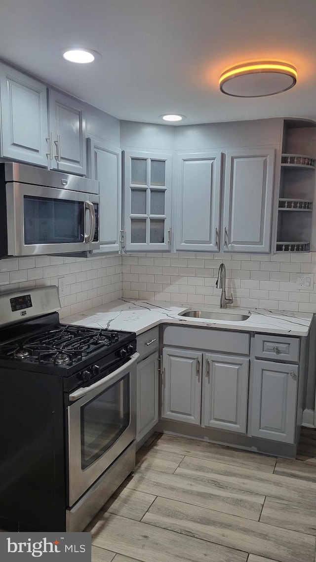 kitchen featuring sink, appliances with stainless steel finishes, light stone countertops, light hardwood / wood-style floors, and tasteful backsplash