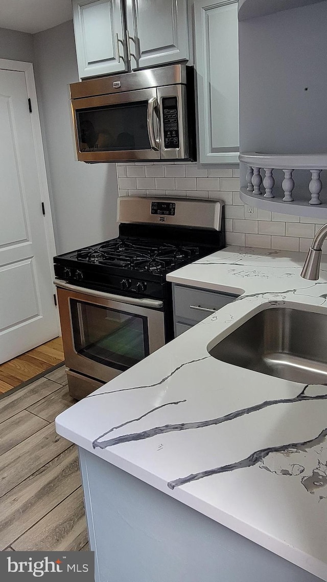 kitchen featuring appliances with stainless steel finishes, backsplash, sink, light stone counters, and light wood-type flooring