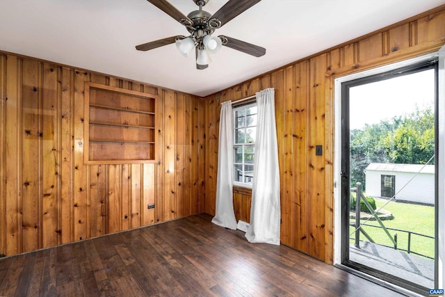 unfurnished room with dark wood-type flooring, wood walls, and ceiling fan