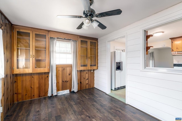 kitchen featuring dark hardwood / wood-style flooring, ceiling fan, white fridge with ice dispenser, and wooden walls