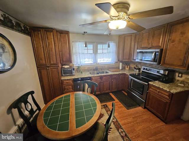 kitchen featuring hardwood / wood-style floors, backsplash, light stone countertops, ceiling fan, and appliances with stainless steel finishes