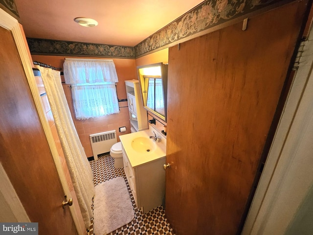 bathroom with toilet, tile patterned flooring, vanity, radiator heating unit, and tile walls