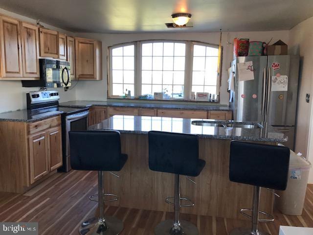 kitchen with appliances with stainless steel finishes, a kitchen breakfast bar, dark hardwood / wood-style flooring, and dark stone countertops