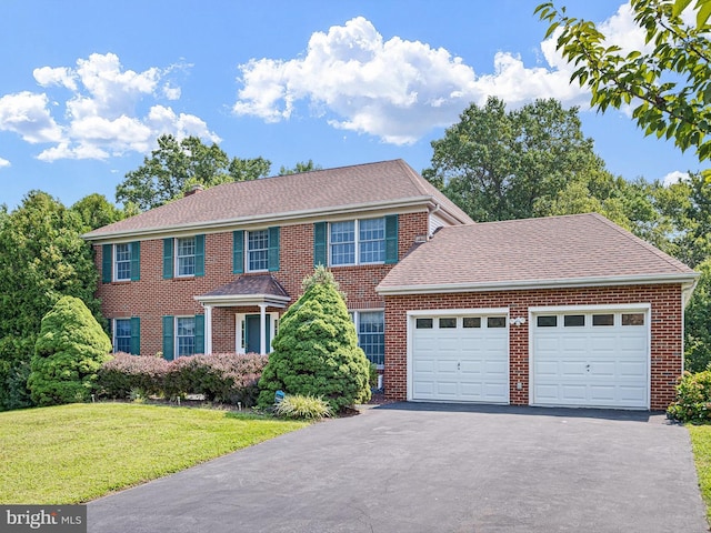 colonial-style house featuring driveway, a front yard, a shingled roof, a garage, and brick siding